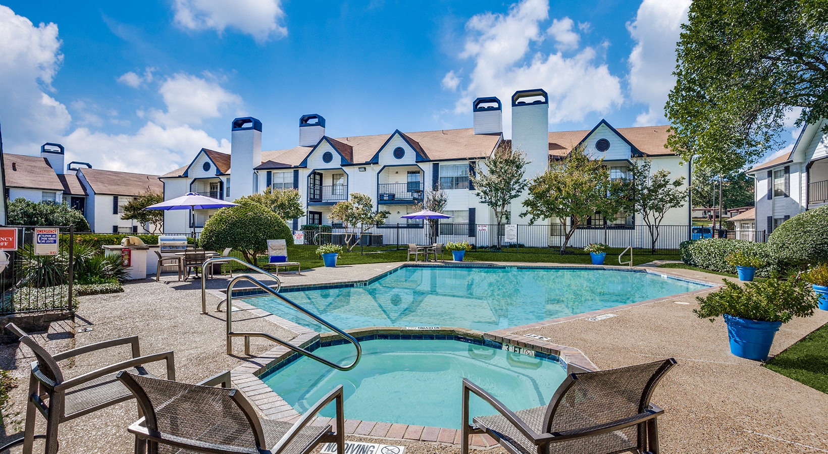 Pool and Hot Tub surrounde by green area and seating, as well as a grill under a parasol